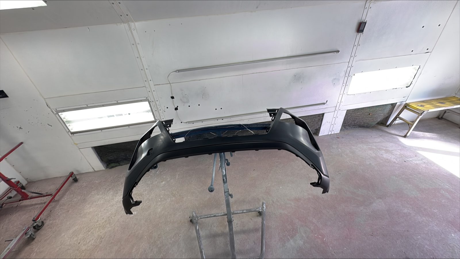 Detached bumper cover positioned on a stand inside the paint booth